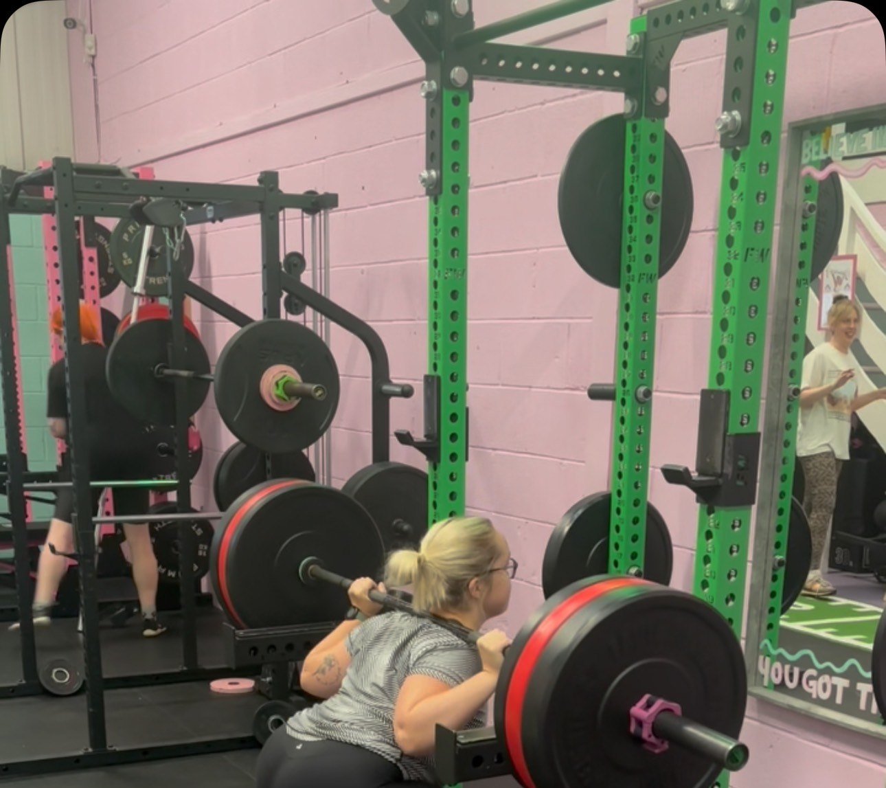 A member bench pressing during PB week, green racks and pink walls behind